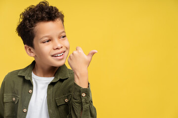 Smiling African American boy pointing to the side with thumb up, isolated on yellow background