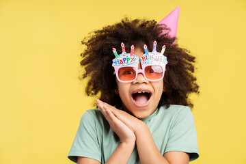 Surprised little girl enjoying her birthday while wearing paper party glasses, posing in studio