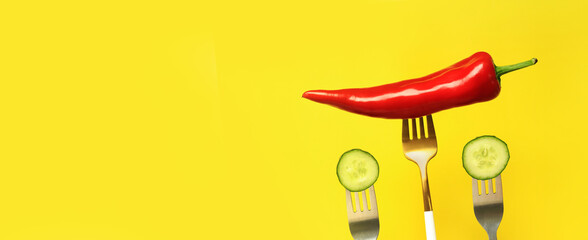 Red pepper and cucumber on forks, yellow background. Hot red pepper and vegetables for salad on a...