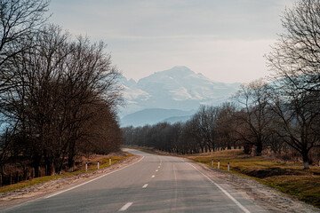 Fototapeta premium the road to the left is an asphalt scenic road with a turn to the left into the mountains with a view of the snow-capped tops of the mountains and a blue sky with clouds and along the road there are a