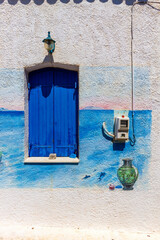 Beautiful local architecture with white washed wall, blue painted window and colorful wall decoration with painted sea and a green flower pot, in Agkistri island, Greece, Europe.