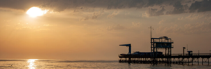 Crane on the sea pier in the rays of the setting sun. Silhouette of a pier on the sea horizon....
