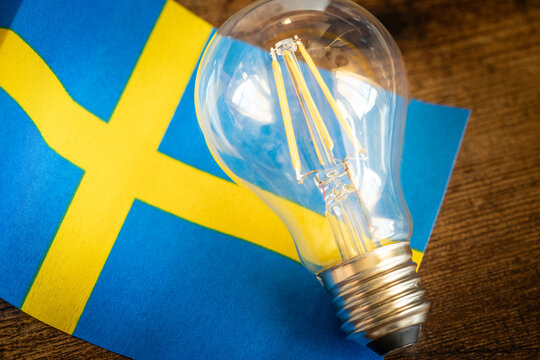 A glowing light bulb lying in the middle of the Swedish flag, Concept, Energy prices in Sweden