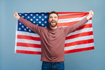 Excited man holding American flag isolated on blue background