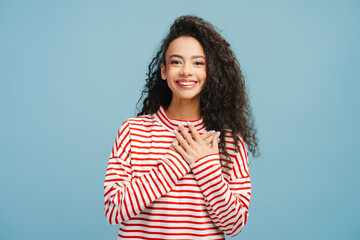 Image of joyful girl, teenager with curly hair pressing her hands to her chest with thankfulness