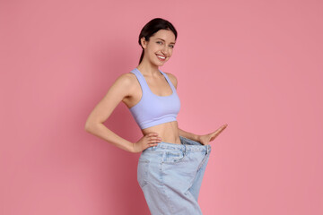 Happy young woman in big jeans showing her slim body on pink background