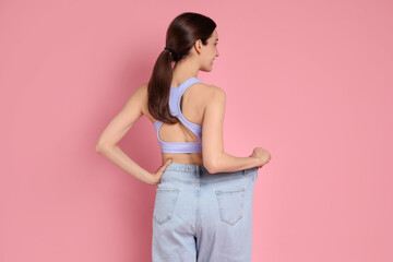 Woman in big jeans showing her slim body on pink background, back view