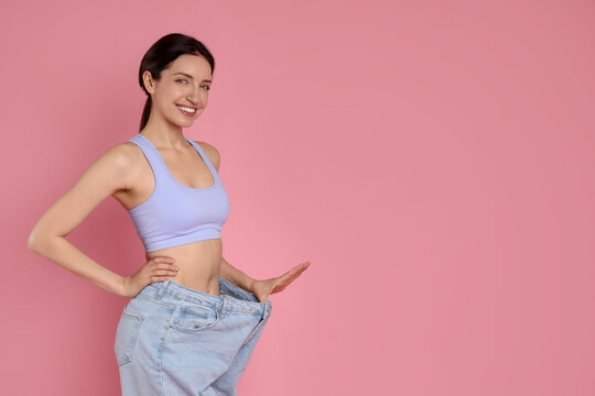 Happy young woman in big jeans showing her slim body on pink background, space for text