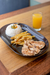 Grilled chicken, accompanied by rice, French fries and orange juice.