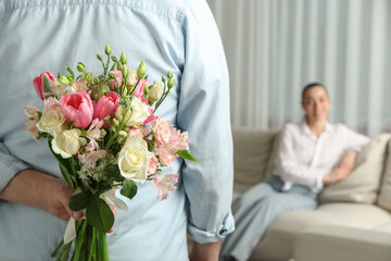 Man hiding bouquet of flowers for his beloved woman indoors, closeup