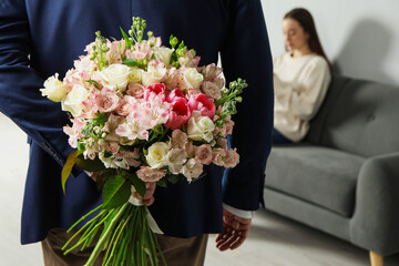 Man hiding bouquet of flowers for his beloved woman indoors, closeup