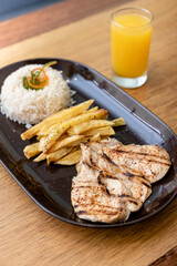 Grilled chicken, accompanied by rice, French fries and orange juice.