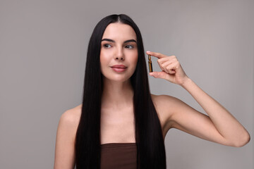 Beautiful young woman holding skincare ampoule on grey background