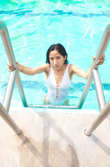 Imagen de una joven mujer delgada saliendo de una piscina por unas escaleras 