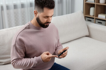 Diabetes test. Man checking blood sugar level with lancet pen on sofa at home