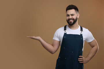 Smiling man in kitchen apron holding something on brown background. Mockup for design