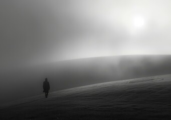 Black and white photo of a person walking alone in a foggy landscape