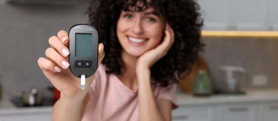 Diabetes. Happy woman holding digital glucometer in kitchen, selective focus