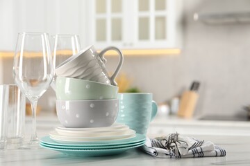 Many different clean dishware, cutlery, glasses and cups on white marble table in kitchen