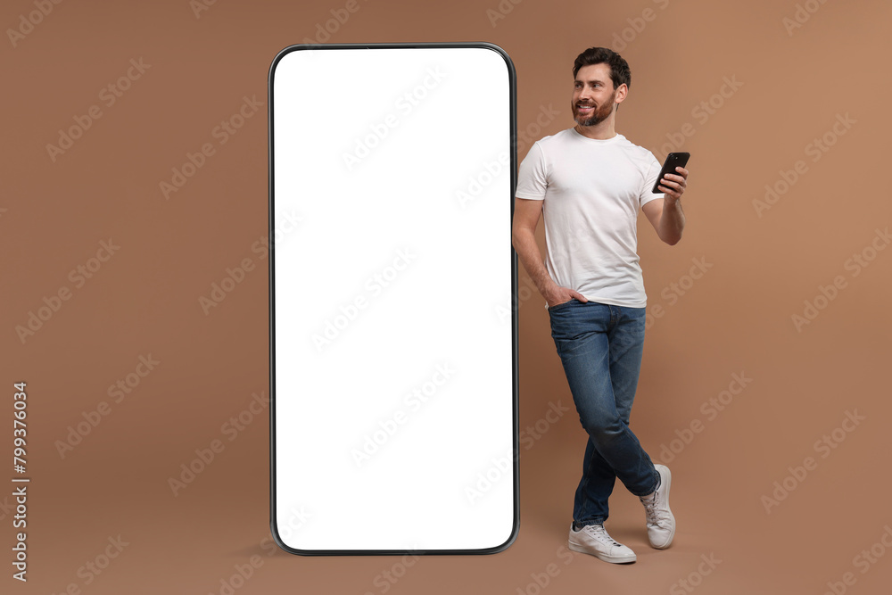 Poster man with mobile phone standing near huge device with empty screen on dark beige background. mockup f