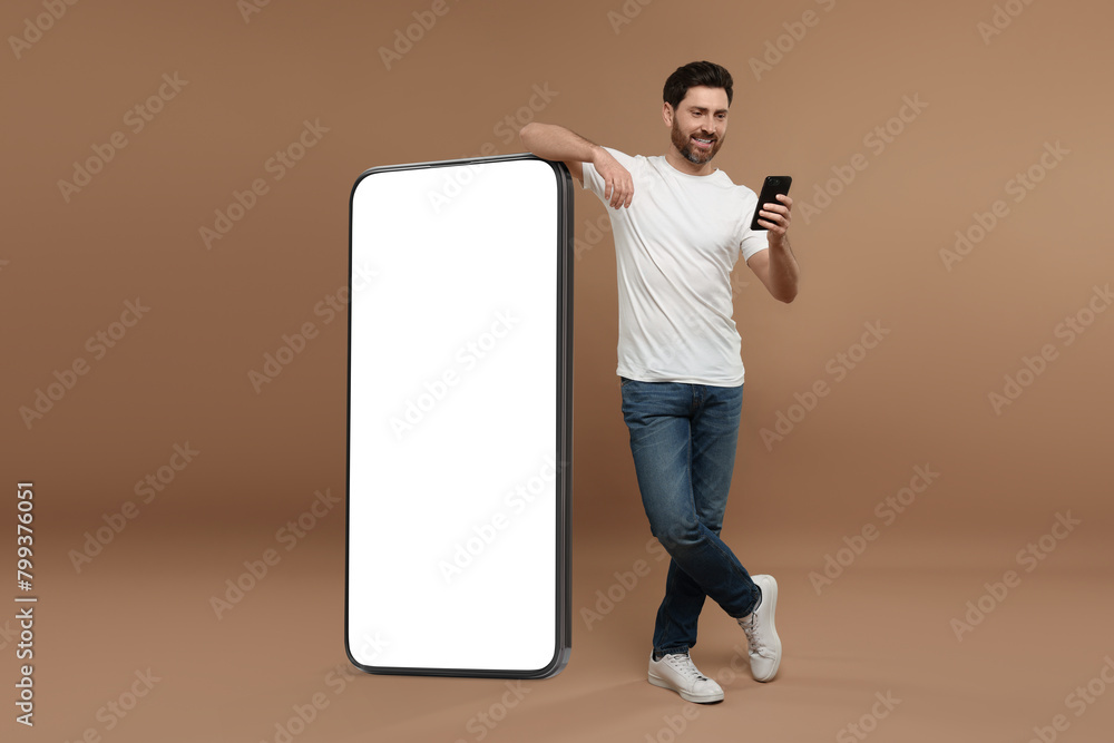 Poster man with mobile phone standing near huge device with empty screen on dark beige background. mockup f