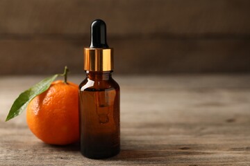 Bottle of tangerine essential oil and fresh fruit on wooden table, closeup. Space for text