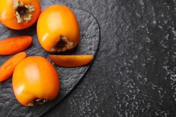 Delicious ripe persimmons on dark textured table, top view. Space for text