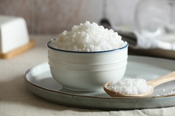 Organic salt in bowl and wooden spoon on table, closeup