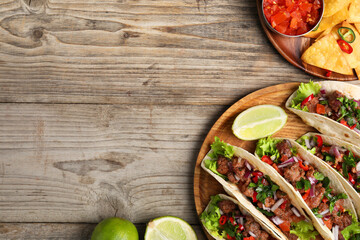 Flat lay composition with delicious tacos on wooden table, space for text