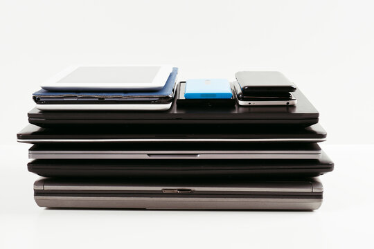 Pile of old used laptop computers, digital tablets, smartphones for recycling on white desk. Donation, technology to charity, e-waste, electronic waste for reuse, upcycling, repair, recycling concept