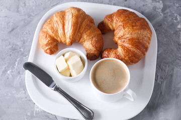 Tasty breakfast. Cup of coffee, fresh croissants, knife and butter on grey table, above view