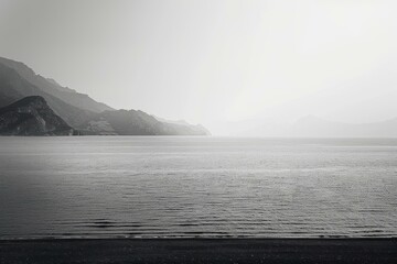 Black and white photo of a calm lake with mountains in the distance