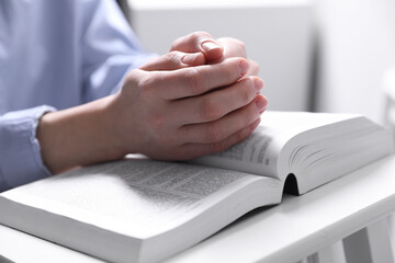 Religion. Christian woman praying over Bible indoors, closeup