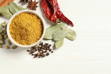 Curry powder in bowl and other spices on white wooden table, flat lay. Space for text