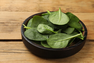 Fresh spinach leaves in bowl on wooden table, closeup