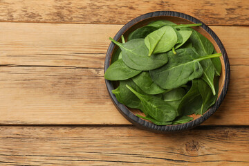 Fresh spinach leaves in bowl on wooden table, top view. Space for text