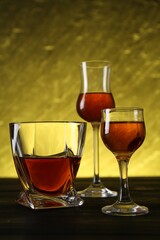 Different delicious liqueurs in glasses on dark wooden table