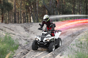 Man driving modern quad bike on sandy road near forest. Light trails showing his speed