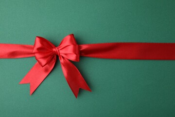 Red satin ribbon with bow on green background, top view