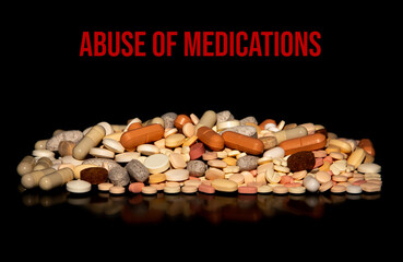 A pile of medication pills on a black background with the inscription ABUSE OF MEDICATIONS. Image representing the abuse of medicines