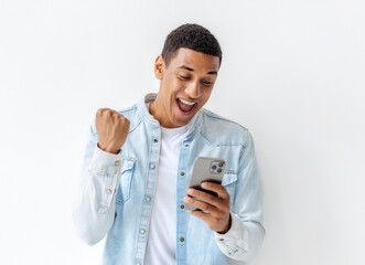 Portrait of a joyful excited  young African American man holding mobile phone standing on a white background