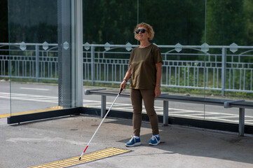 An elderly blind woman is waiting for transport at a bus stop.