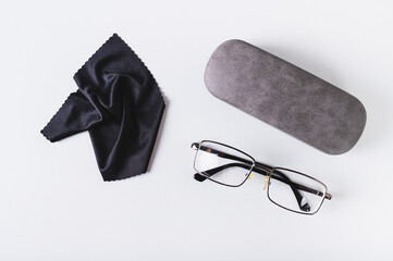 Metal frame eyeglasses, hard case and cleaning cloth on blue background top view