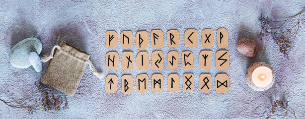Scandinavian runes for fortune telling, pouch and candle on the table top view web banner