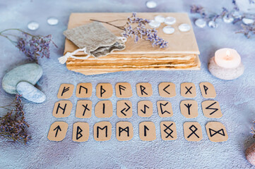 Scandinavian runes for fortune telling are  in three rows, a book, stones and a candle on the table