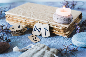 Fortune telling cardboard runes next to an old book, a candle and stones on the table