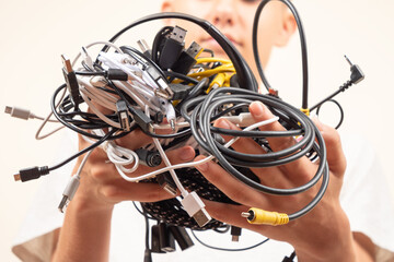 Teenager hands holding pile of tangled old smart technology wires, used charging cables and cords. E-waste, planned obsolescence, electronic donation, disposal of electronic waste, recycling concept