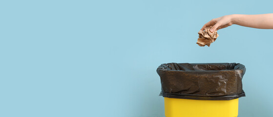 Female hand throwing crumpled paper into trash bin near blue wall