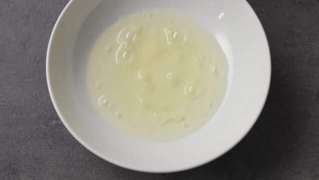 Chef pours raw egg white into white bowl, top view. Close-up of food