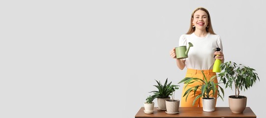 Beautiful young woman with watering can, sprayer and houseplants on table against grey background with space for text